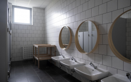 Na zdjęciu widać łazienkę w nowym żłobku, nisko usytuowane umywalki, a nad nimi okrągłe lustra w drewnianych ramach