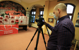 Realizator z kamerą filmuje ustawione na stole prezenty różnej wielkości, opakowane w biay papier z delikatnym złotym wzorkiem i z czerwonymi kokardami