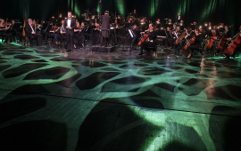 Toruńska Orkiestra Symfoniczka podczas koncertu noworocznego, na pierwszym planie światł oświetlają scenę