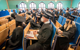 Absolwenci w biretach siedzą w ławkach auli Kolegium Jagiellońskiego