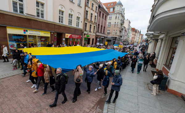 Na zdjęciu: ludzie niosą ulicą miasta żółto-niebieską flagę Ukrainy