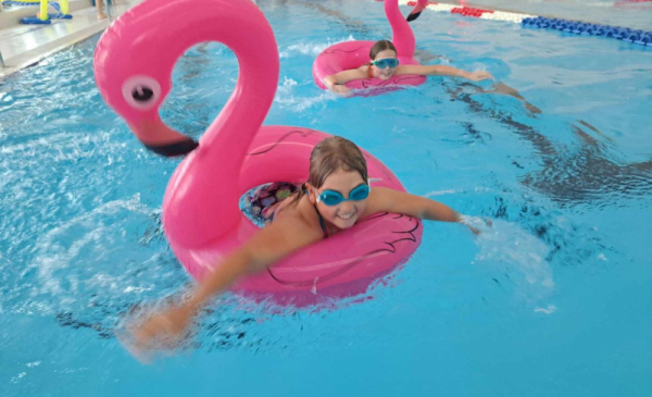 Na zdjęciu: dwie dziewczynki w kołach w kształcie różowego flaminga pływają w basenie