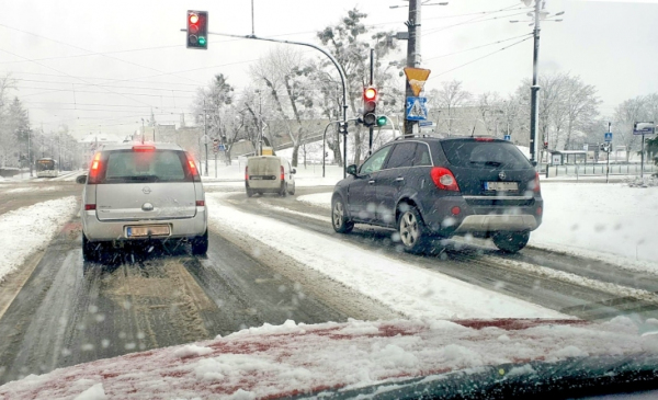 Na zdjęciu samochody stoją na skrzyżowaniu, pada śnieg