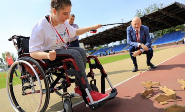 Dziewczynka na wózku podczas Toruńskiej Olimpiady Osób Niepełnosprawnych, w tle prezydent Torunia