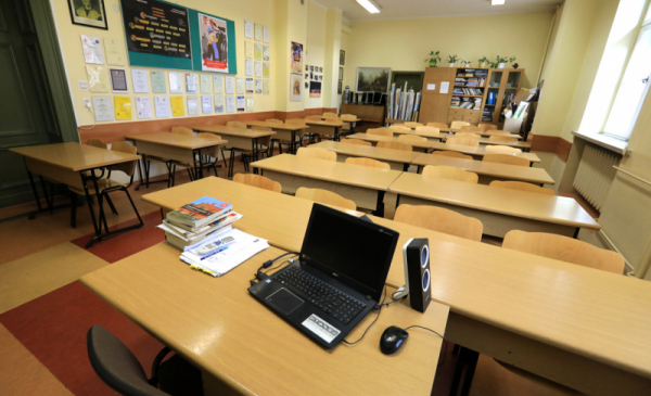 Klasa lekcyjna z pustymi ławkami i laptopem na biurku nauczyciela