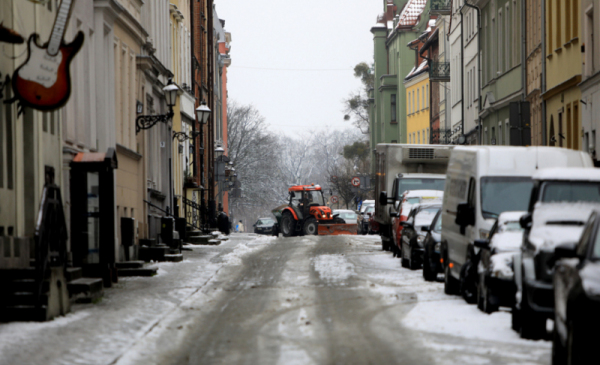 Zdjęcie przedstawia zaśnieżoną ulicę Torunia, na której znajduje się pług śnieżny