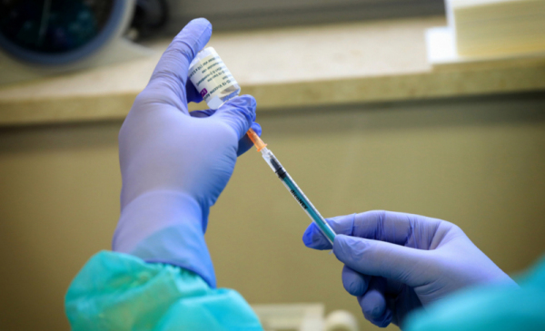 Na zdjęciu osoba w rękawiczkach pobiera szczepionkę do strzykawki