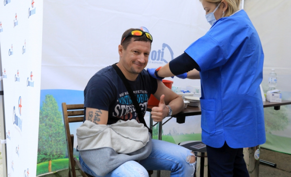 Na zdjęciu uśmiechnięty mężczyzna jest szczepiony i pokazuje kciuk w górę