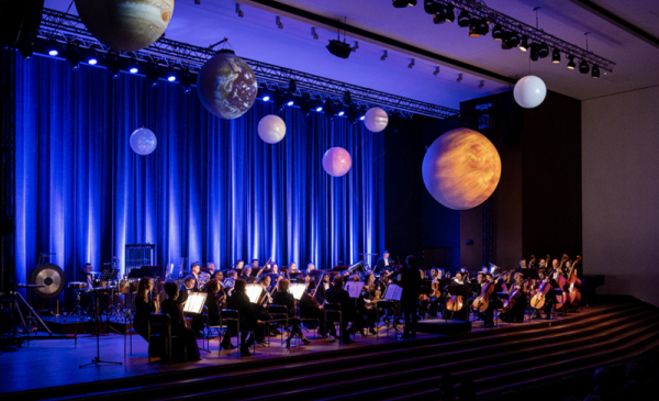 Koncert "Muzyka i kosmos" w Auli UMK: orkiestra na scenie udekorowanej planetami
