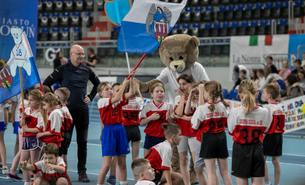Na zdjęciu: dzieci w hali sportowej stoją z flagą miasta