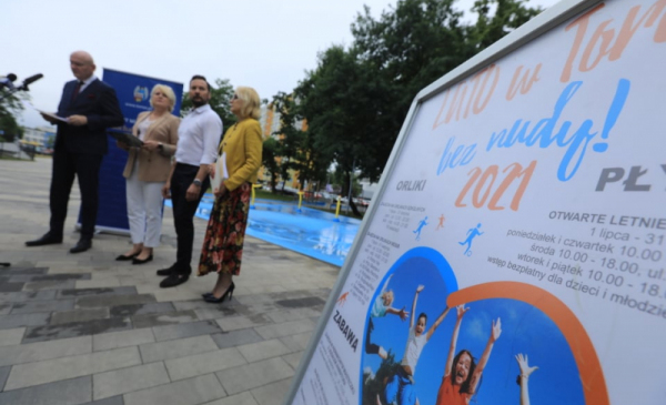 Na pierwszym planie fragment plakatu "Lato w Toruniu bez nudy, w tle uczestnicy konferencji prasowej