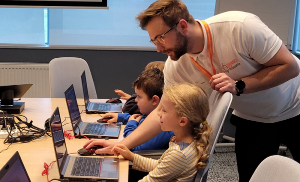 Na zdjęciu: mężczyzna tłumaczy dzieciom pracującym na komputerach