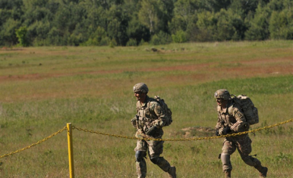 Dwóch żołnierzy biegnie po łące na terenie poligonu