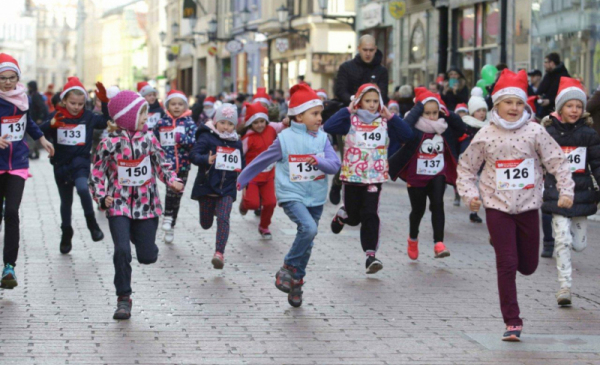 Zdjęcie przedstawia dzieci w czapkach św. Mikłaja biegnące ulicą Szeroką