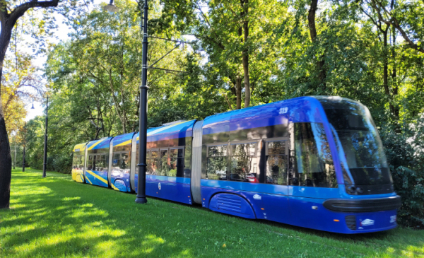 Na zdjęciu: niebieski tramwaj jedzie po torowisku porośniętym trawą