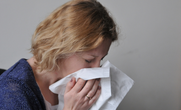 Na zdjęciu kobieta wydmuchuje nos w chusteczkę higieniczną