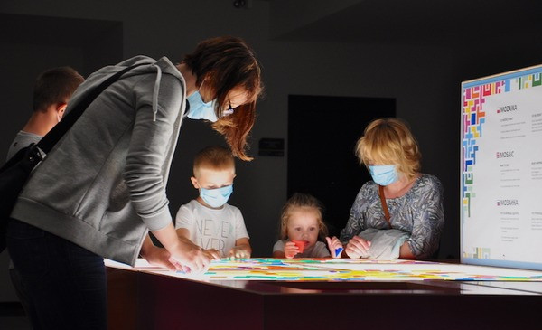 Kobieta i troje dzieci w maseczkach sa pochyleni nad tablicą interaktywną w Centrum Nowoczesności Młyn Wiedzy