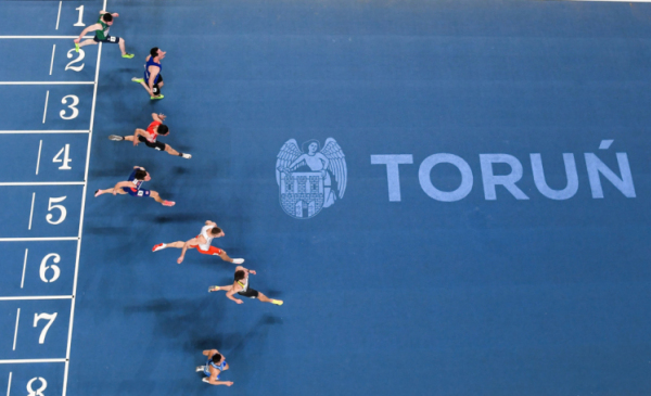 Na zdjeciu: biegacze wbiegają na metę w hali Arena Toruń, na nawierzchni napis Toruń i herb miasta