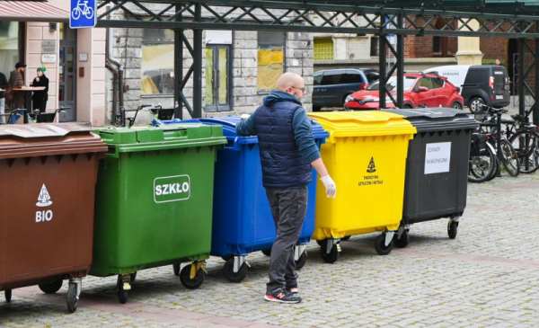 Zdjęcie przedstawia mężczyznę na tle pojemników na odpady.