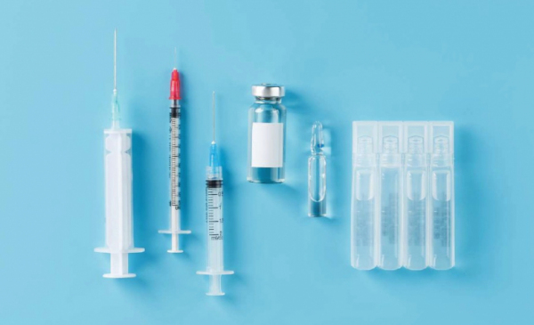 Na zdjęciu strzykawki z ampułkami ze szczepionką na niebieskim tle