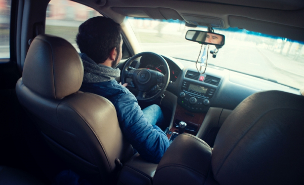 Na zdjęciu mężczyzna ubrany niebieską kurtkę siedzi wewnątrz samochodu podczas jazdy