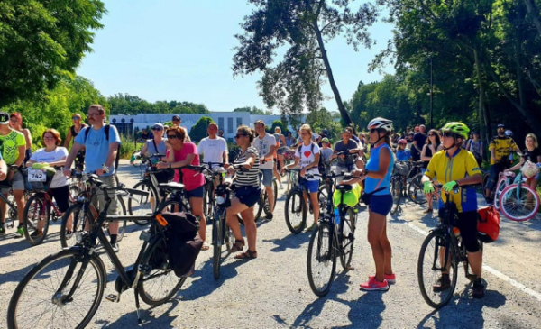 Na zdjęciu grupa rowerzystów stoi z rowerami i słucha przewodnika