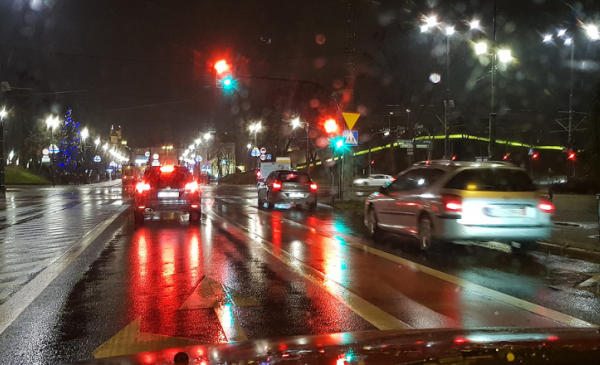 Na zdjęciu samochody stoją przed skrzyżowaniem, pada deszcz