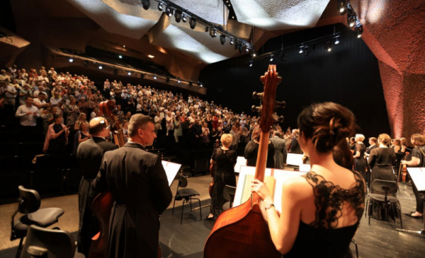 Na zdjęciu: zza pleców muzyków Toruńskiej Orkiestry Symfonicznej widać publiczność bijącą brawo na stojąco