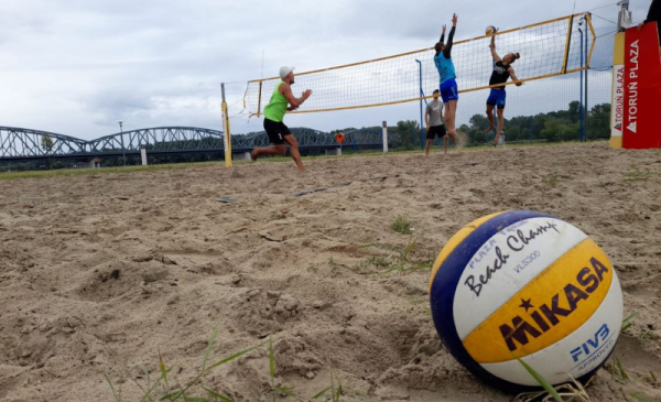 Na zdjęciu: mecz piłki siatkowej plażowej, na pierwszym planie na piasku leży piłda do gry w siatkówkę