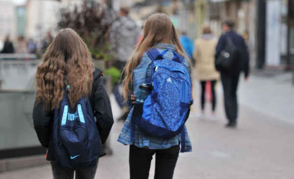 Na zjęciu: dwie długowłose dziewczynki idą z plecakami szkolnymi na plecach