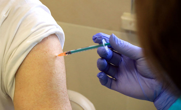Na zdjęciu zbliżenie na strzykawkę ze szczepionką podczas podawania zastrzyku - widać ramię i wkłutą igłę