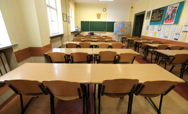 Na zdjęciu widać salę klasową, puste ławki i krzesła, z przodu na ścianie wisi tablica
