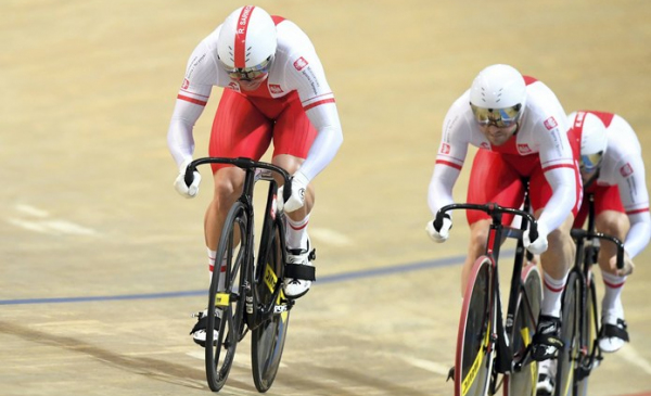 Na zdjęciu: zawodnicy kolarstwa torowego w białoczerwonych strojach na rowerach startują na torze w hali