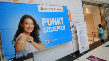 Na zdjęciu baner z uśmiechniętą kobietą i napisem Punkt Szczepień Toruń Plaza