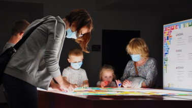 Kobieta i troje dzieci w maseczkach sa pochyleni nad tablicą interaktywną w Centrum Nowoczesności Młyn Wiedzy