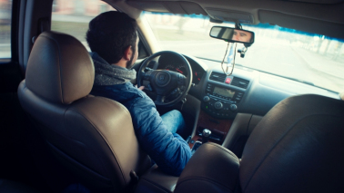 Na zdjęciu mężczyzna ubrany niebieską kurtkę siedzi wewnątrz samochodu podczas jazdy