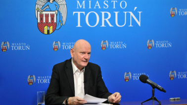 Prezydent Michał Zaleski podczas zdalnej sesji Rady Miasta Torunia, w tle herb miasta