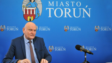 Prezydent Michał Zaleski na tle niebieskiej ścianki promocyjnej z herbem Torunia