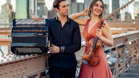 mężczyzna z akordeonem i kobieta ze skrzypcami w długiej, eleganckiej sukience, w tle Nowy Jork