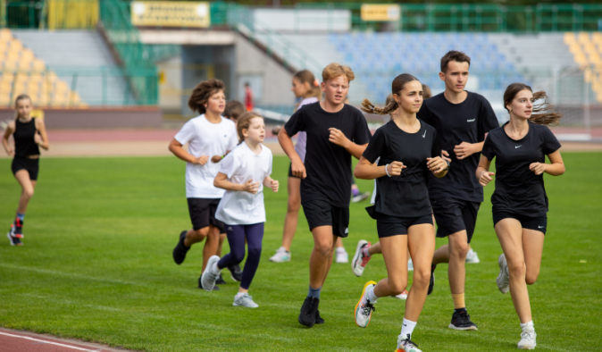 Na zdjęciu: grupa młodzieży biegnie po zielonej murawie stadionu