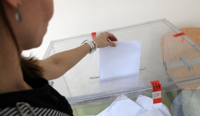 Na zdjęciiuL kobieta wrzuca złożoną kartę do głosowania do urny wyborczej