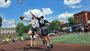 Na zdjęciu: koszykarze grają na boisku zewnętrznym, w tle budynek szkoły