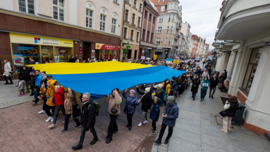 Na zdjęciu: ludzie niosą ulicą miasta żółto-niebieską flagę Ukrainy