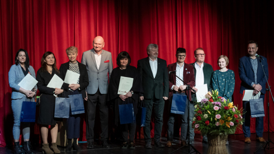 Na zdjęciu: osoby nagrodzone z okazji Międzynarodowego Dnia Teatru stoją na scenie na tle czerwonej kurtyny