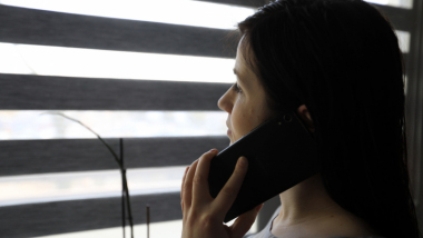 Dziewczyna rozmawiająca przez telefon komórkowy przy oknie z żaluzjami
