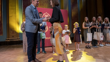 Na zdjęciu: zastępca prezydenta Artur Szponka wręcza nagrodę nastolatce, z tyłu stoja pozostali uczestnicy konkursu wokalnego