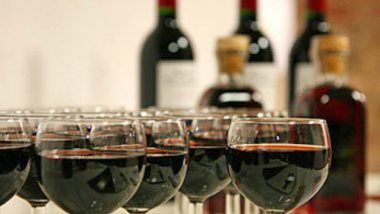 Na zdjęciu: kieliszki napełnione czerwonym winem, w tle trzy butelki wina