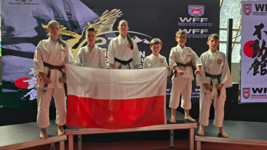 Na zdjęciu: zawodnicy karate w białych strojach stoją na podium i trzymają polską flagę
