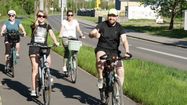 Na zdjęciu uśmiechające się osoby jadą na rowerze