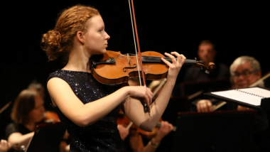 Na zdjęciu młoda solistka gra na skrzypcach podczas koncertu